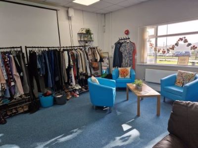 A room with blue chairs, a table and clothes on a rack in the background